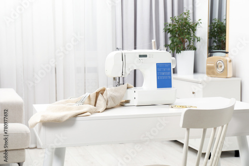 Sewing machine, measuring tape, scissors and fabric on white desk in workshop