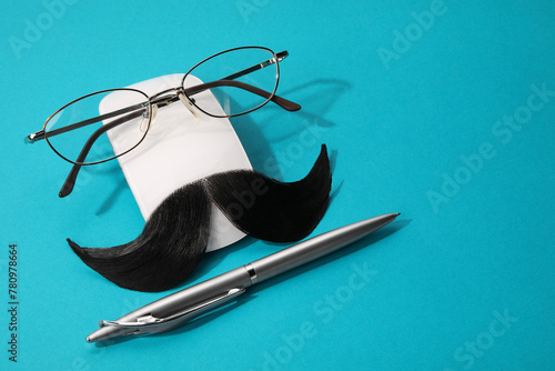 Composition with artificial moustache and glasses on light blue background, space for text photo