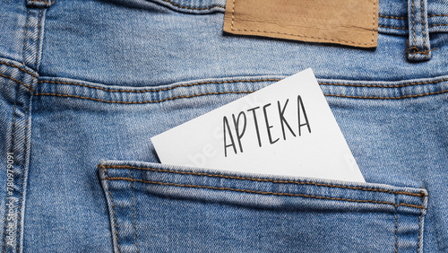 White card with a handwritten inscription "Apteka", inserted into the pocket of blue pants jeasnow (selective focus), translation: Pharmacy