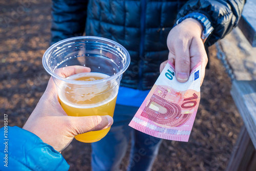 A hand is holding 10 europe in exchange for a cup of beer. Money exchange is common activities to tourists. Small bills are preferable for public transportation or vehicle rental, groceries, pub, bar