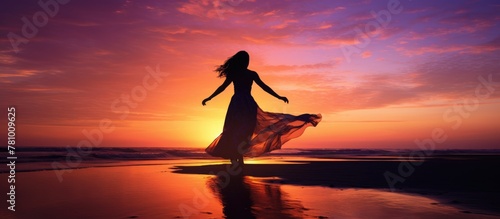 A lady in an elegant, floor-length dress stands gracefully on the beach as the sun sets in the background