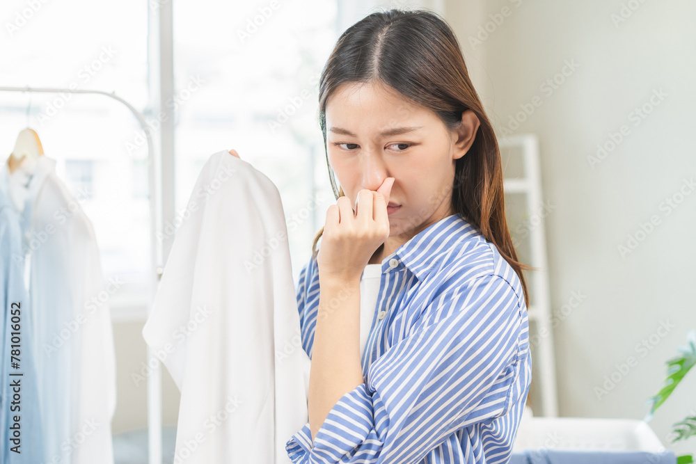 Asian young housewife woman having bad smelling clothes hand holding breath nose with finger, sniff smelly dirty stinky musty, look disgusting from clothes after washed, laundry out of machine at home Asian young housewife woman having bad smelling clothes hand holding breath nose with finger, sniff smelly dirty stinky musty, look disgusting from clothes after washed, laundry out of machine at home