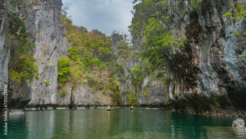 Canoes with tourists sail along a calm emerald lagoon surrounded by karst rocks. Green tropical vegetation on steep slopes. Reflection. Small lagoon. Philippines. Miniloc Island. Palawan photo