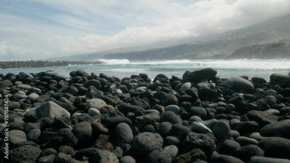 Slowmotion group of surfers revealed behind stones on pebble beach, Playa Martiánez, Puerto de la Cruz, Tenerife, Canary Islands in spring Slowmotion group of surfers revealed behind stones on pebble beach, Playa Martiánez, Puerto de la Cruz, Tenerife, Canary Islands in spring