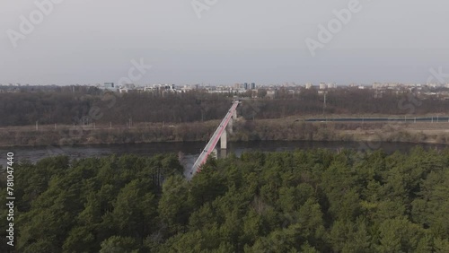 A drone flight begins above a dense forest and moves towards a bridge, revealing its full span as it connects over the river towards the city. photo