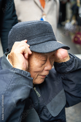 An old Asian man buys, selects and tries on hats at the market