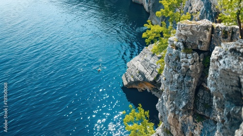 A swimmer diving off a rocky cliff into a deep blue lake below.