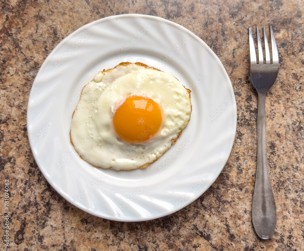 Fried egg on a white plate with a fork on the table Fried egg on a white plate with a fork on the table