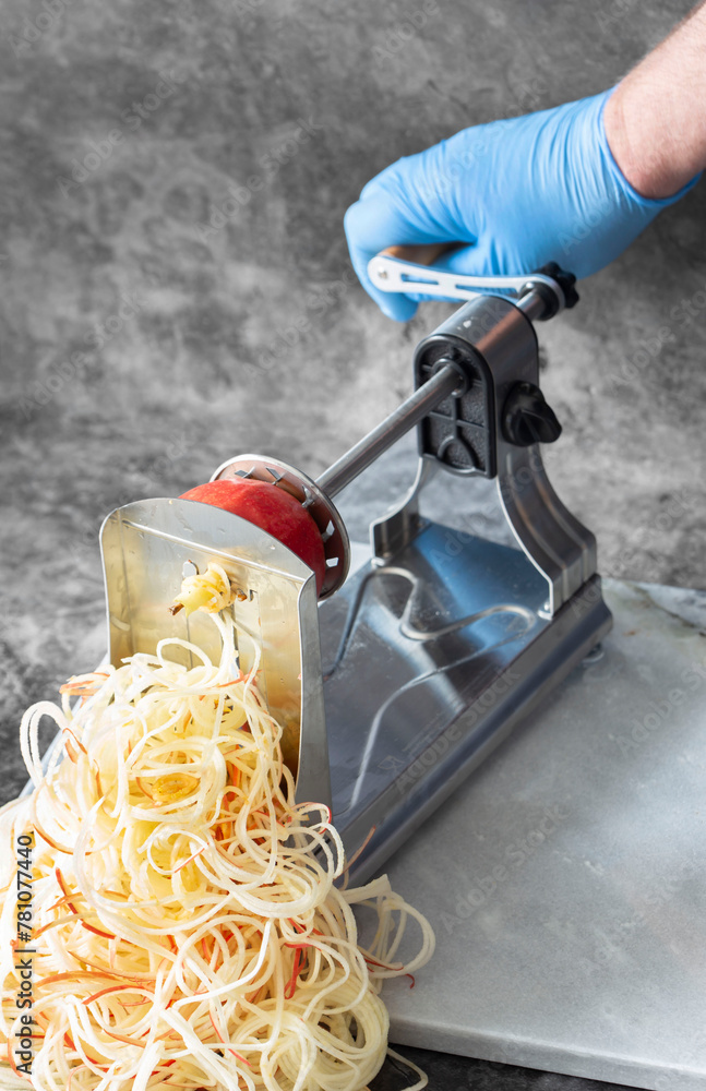 Man using spiralizer to cut apple into strips. On a dark stone background