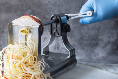 Man using spiralizer to cut apple into strips. On a dark stone background