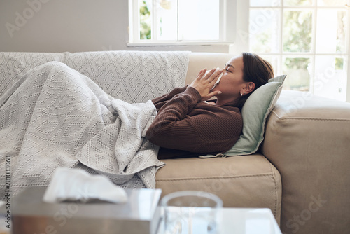 Sick woman, sneeze and blowing nose with flu, cold or illness on living room sofa at home. Young female person with tissue for bacteria, fever or influenza in fatigue or rest on lounge couch at house