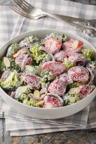 Fresh broccoli salad with strawberries, red onions and almonds dressed with yogurt close-up in a plate on the table. Vertical