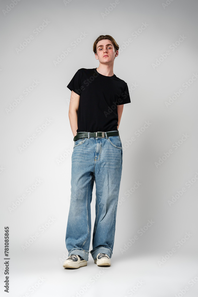 Casual Young Man Posing in Black T-Shirt and Blue Jeans Against a Plain Background Casual Young Man Posing in Black T-Shirt and Blue Jeans Against a Plain Background