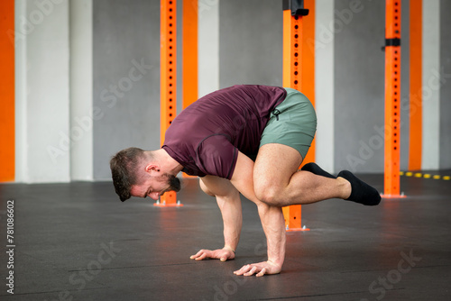 Strong man performing calisthenics frog stand exercise in gym