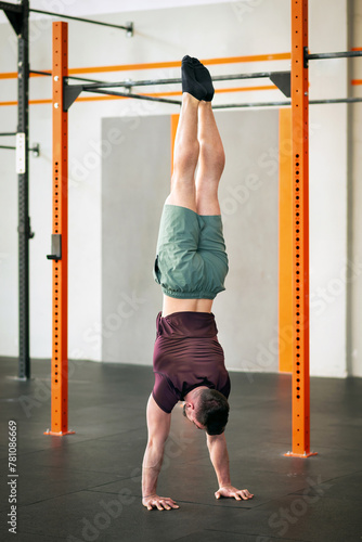Determined sportsman performing calisthenics handstand position at gym