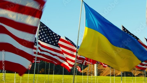 4k high quality footage. View on Ukraine and American flags waving in the wind against green grass in nature background on sun. Concept of 4th of July, Memorial Day, Independence Day, September 11.