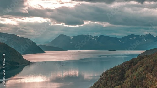 Rays of the setting sun shine through the storm clouds above the serene fjord in a timelapse video. photo