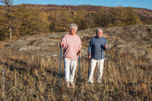 Happy middle age woman and man walking with Scandinavian sticks in autumn forest