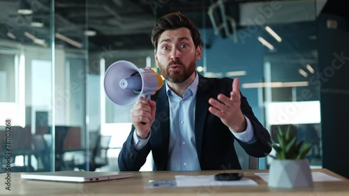 Amazed business person shouting through bullhorn and gesturing actively while sitting alone by desktop. Creative entrepreneur waving hand while talking to camera with funky accessory at workspace. photo