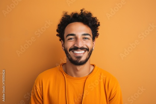 A man with a beard and a smile is wearing an orange shirt