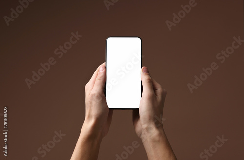 Man holding smartphone with blank screen on brown background, closeup. Mockup for design