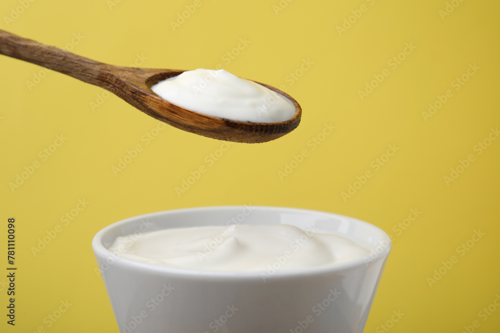 Eating delicious natural yogurt on yellow background, closeup