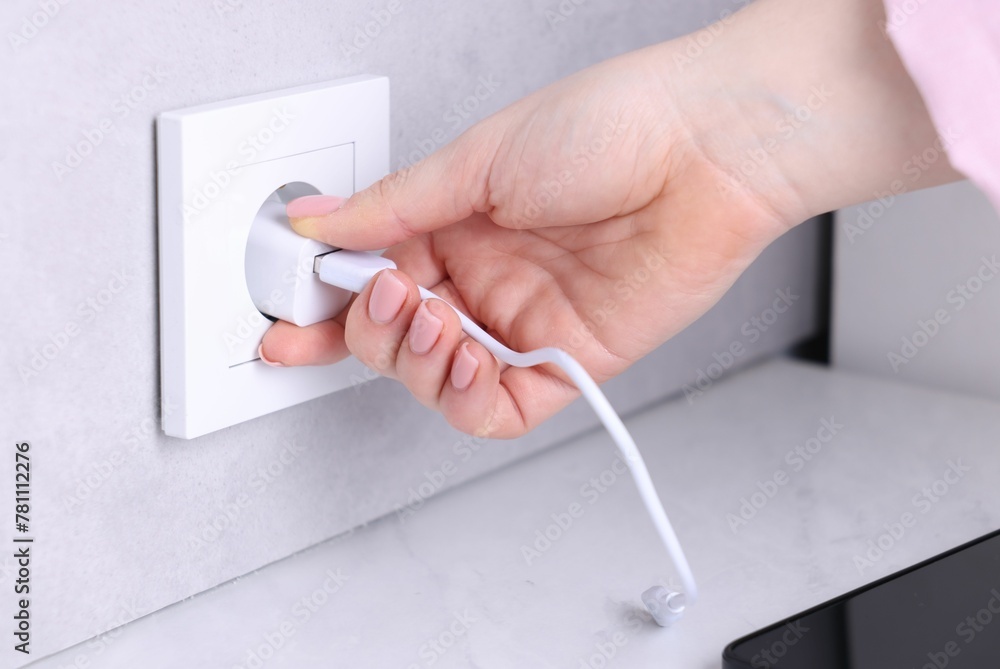 Woman plugging smartphone into power socket at white table indoors, closeup Woman plugging smartphone into power socket at white table indoors, closeup