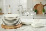 Clean plates, glasses and butter dish on white marble table in kitchen