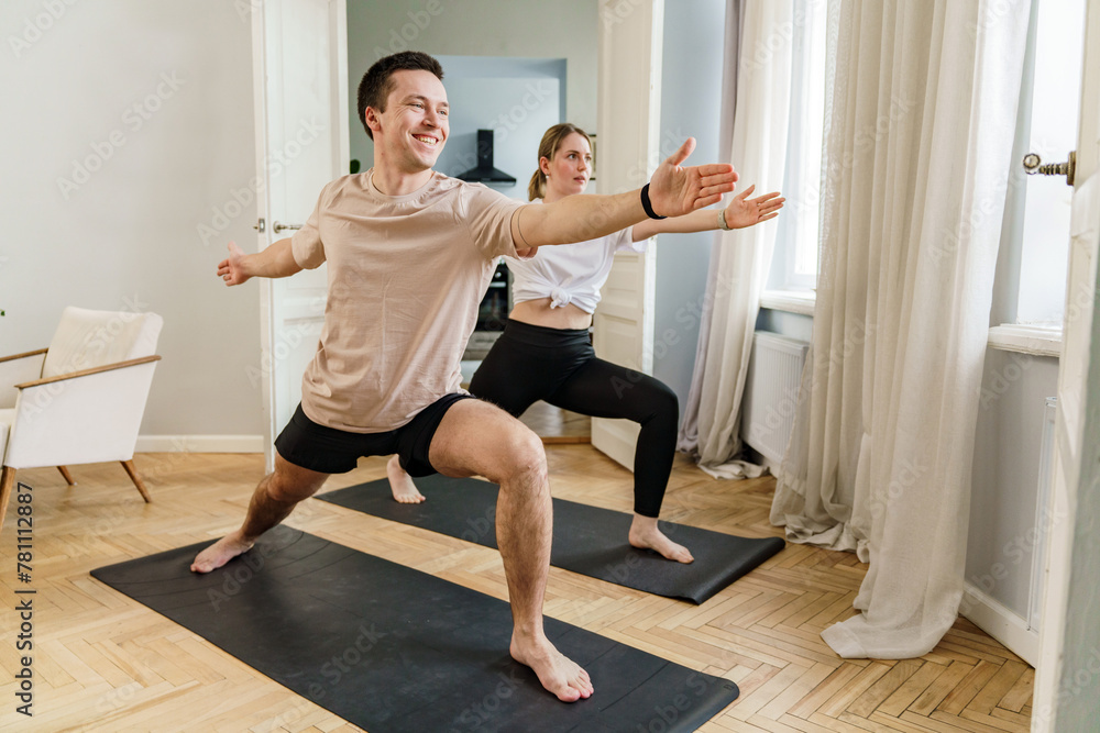 Fototapeta premium A couple energetically engages in a yoga pose, smiling as they stretch and maintain balance, capturing the essence of a healthy, active lifestyle at home.