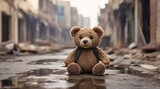 Sad abandoned little teddy bear sitting on the ground in the destroyed street after war or earthquake. Human suffering and concept of destroying childhood by war.