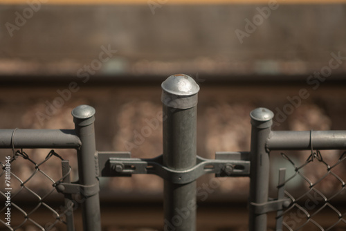 Closeup of the top of a chain link fence. in the defocused background, a train track is visible.