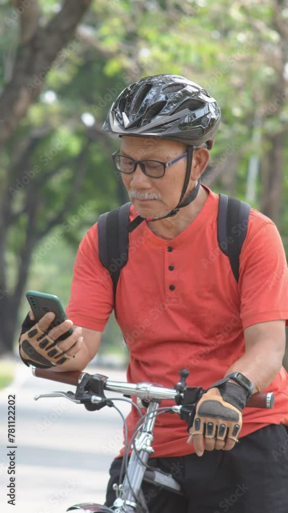 Mature Man in Orange Shirt and Cycling Helmet Checking Smartphone While Resting on Bike Mature Man in Orange Shirt and Cycling Helmet Checking Smartphone While Resting on Bike