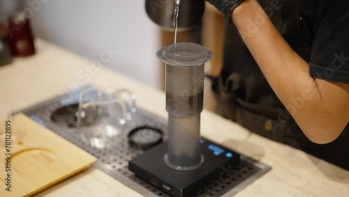 Barista presses signature Aeropress coffee in coffeeshop. Manual brewing method, pouring water with teapot in aeropress bulb. photo
