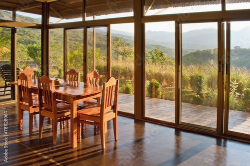 Wooden table in the house interior. Large glass windows and view into the landscape.