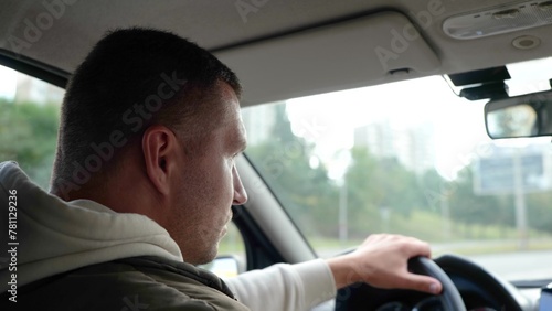 Handsome Caucasian adult man driving a car on highway and looking on sides. Rear view. Close up. Male holding hand on steering wheel drives a vehicle in city. Driver travels in auto © Nataliya