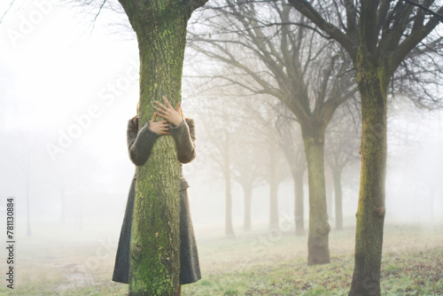 hands touch the trunk of a tree, embracing it in a grove surrounded by fog