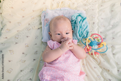 Infant Baby Girl is laying on her back in a pink bodysuit grasping her hands in her mouth while teething.
