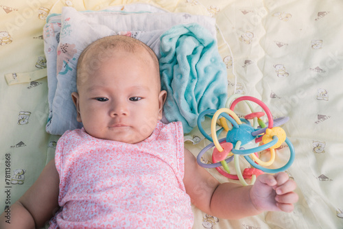 Infant Baby Girl is laying on her back in a pink bodysuit with a development toy for teething.