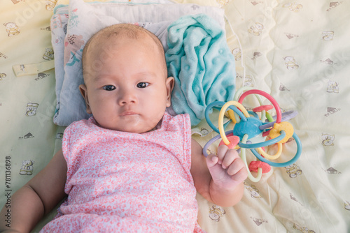 Infant Baby Girl is laying on her back in a pink bodysuit with a development toy for teething.