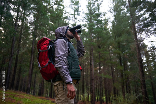 Bird watching, woods and man with binocular, travel and hiking with trees and adventure with hobby. Person, forest and guy with freedom or wellness with hiker and explore nature with journey or peace