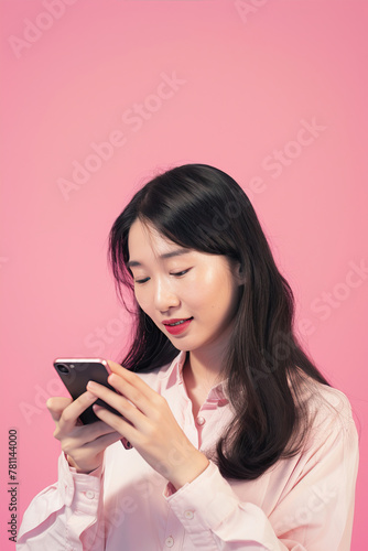 Woman on a pink background looks at the phone and smiles
