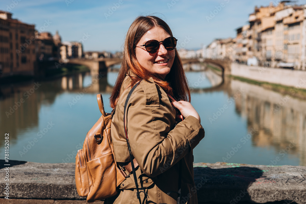 Stylish Happy Young woman enjoys beautiful view on famous Old bridge in Florence. Female traveler visiting Italian landmarks. Concept of travel, tourism and vacation in city