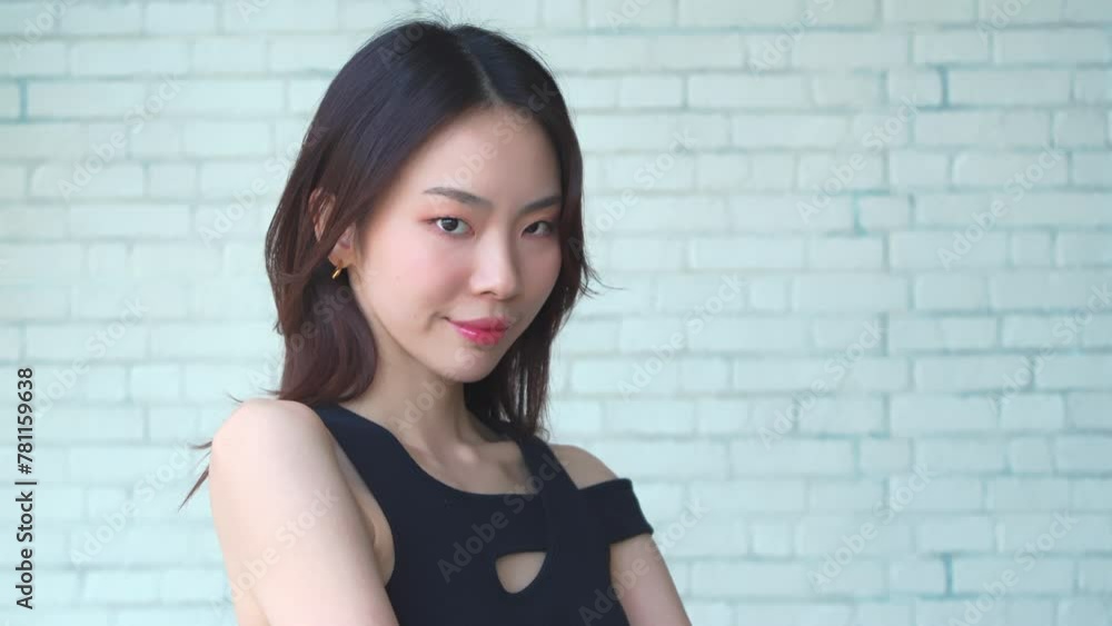 Confident young Asian woman with a subtle smile against a brick wall backdrop Confident young Asian woman with a subtle smile against a brick wall backdrop