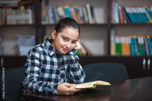 beautiful schoolgirl sitting in the library and reading a book