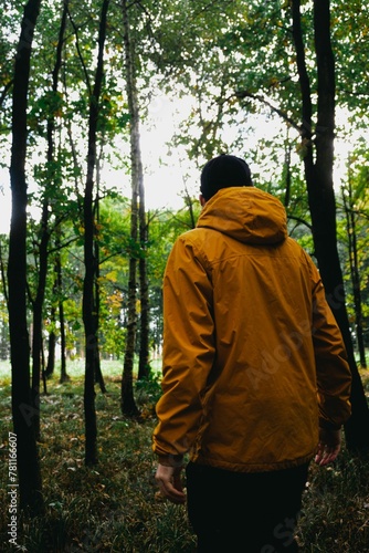 Vertical back view of the traveler with an orange coat walking in the lush forest