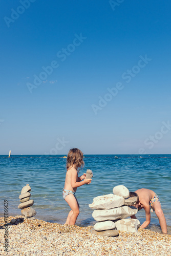 Children play on the seashore. A little girl and boy play with stones on the beach on a sunny summer day