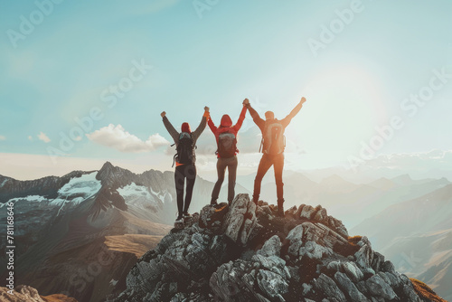 Triumphant trio of hikers holding hands on a mountain peak at sunrise photo