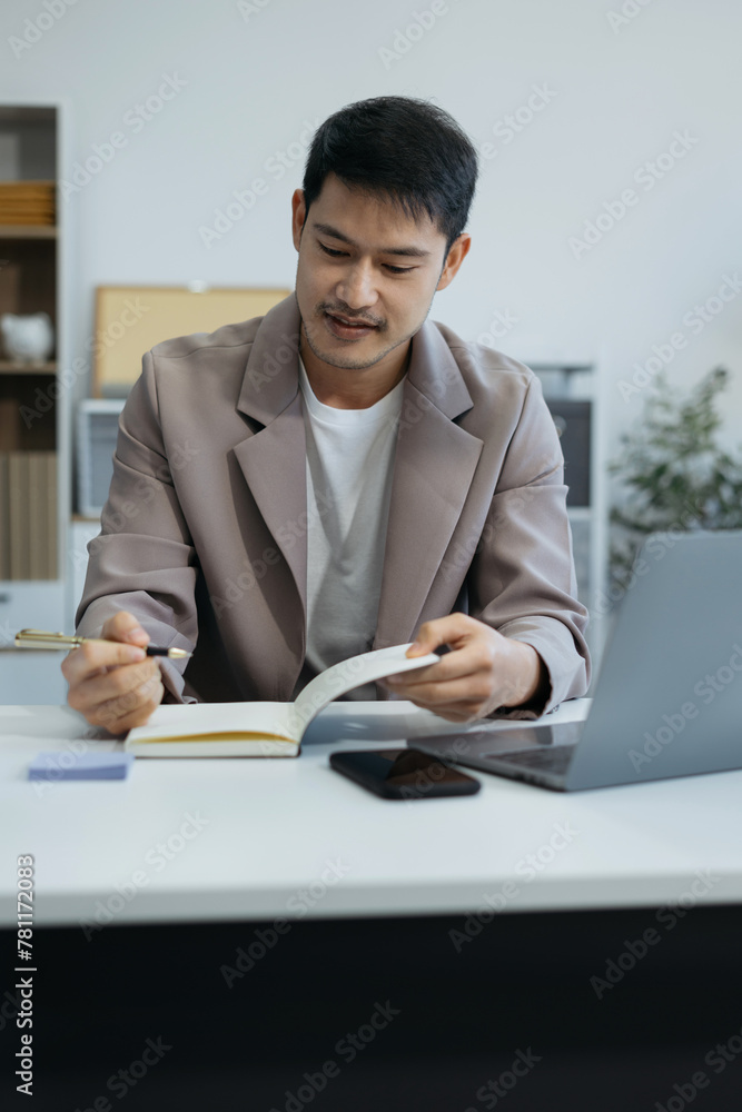 Businessman sitting at a table at office working on a laptop and writing down ideas in a notebook. Businessman sitting at a table at office working on a laptop and writing down ideas in a notebook.