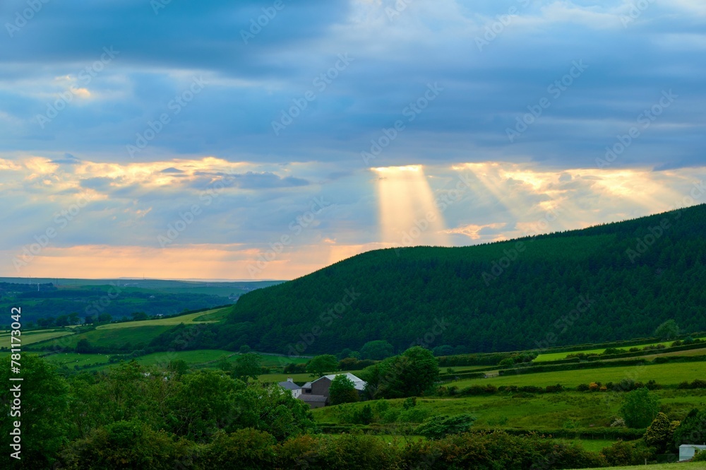 Scenic view of bright rays of sunlight breaking through clouds over evergreen mountains in Cumbria