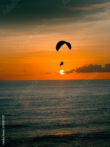 Silhouette shot of a person paragliding above a coast on a sunset